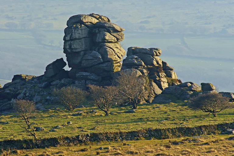 Green moorland with grey granite rocky outcrop in centre of frame, Dartmoor green fields in background