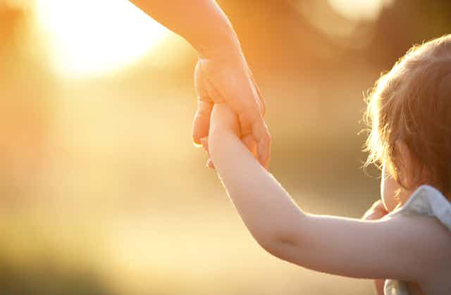 Close up of a parent's hand holding a child's hand, with sun shining in the background