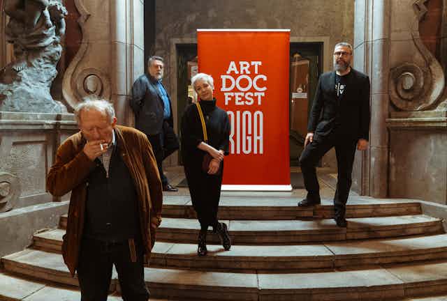 Four people stand in front of a sign for Art Doc Fest Riga