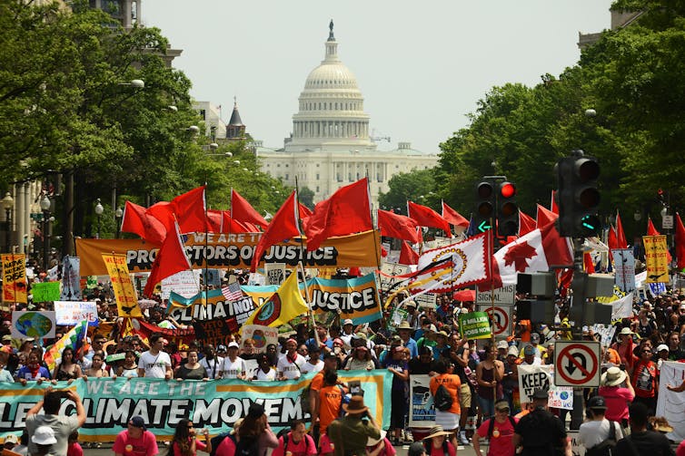 A large crowd of people march and wave banners and flags in front of the US Capitol building.