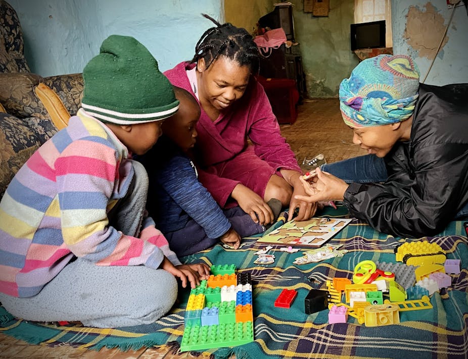 Two adult women play with puzzles, showing pieces to two small children who are not facing the camera