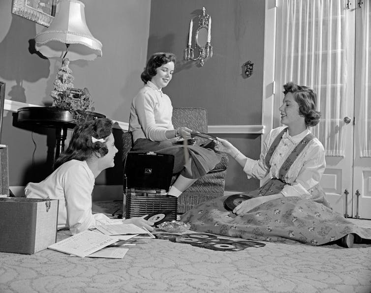 Photo from the 1950s of three teenage girls relaxing on a carpet listening to records.
