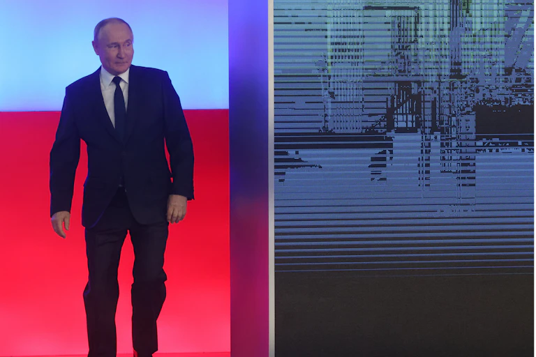 A man in a dark suit walks out from behind a wall.