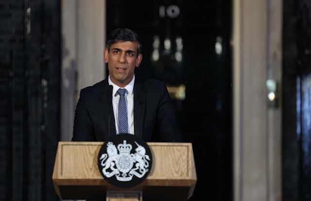 Rishi Sunak standing at a lectern in front of 10 Downing street in the dark