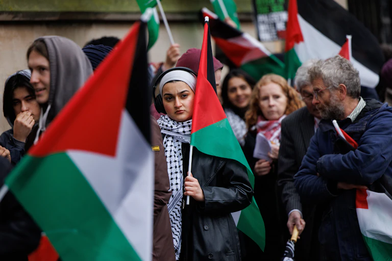 Protesters walking in London carrying large Palestinian flags.