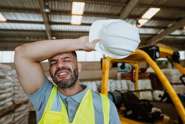 A warehouse worker wears a yellow safety vest and an expression of exhaustion.