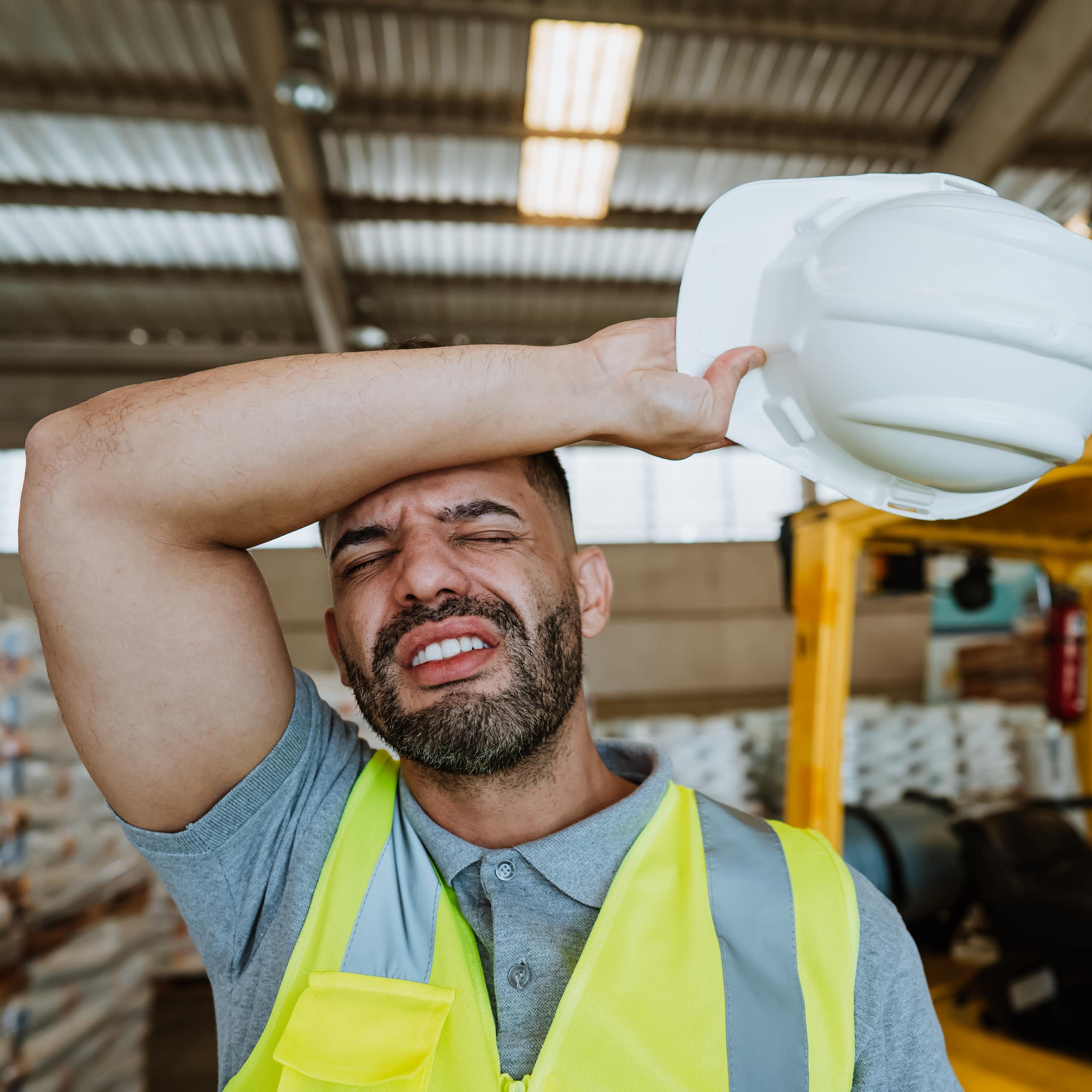 A warehouse worker wears a yellow safety vest and an expression of exhaustion.