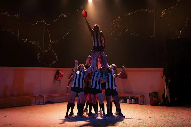 The cast on stage, reaching for a football