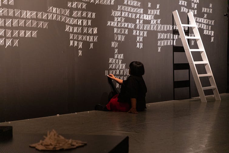 A woman paints counting marks on a wall.