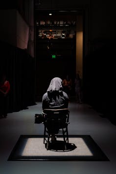 A man sits with a covered head.