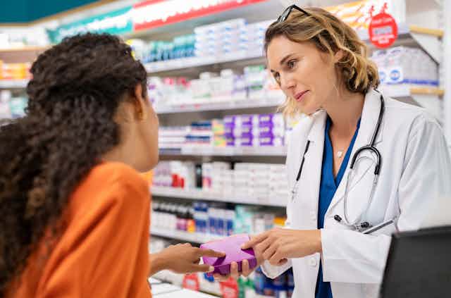 Pharmacist talks to customer over the counter. Both appear female