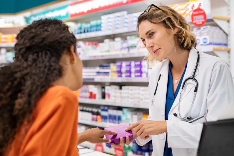 Pharmacist talks to customer over the counter. Both appear female