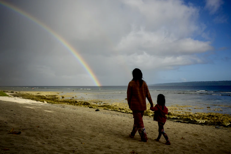 woman and child walk on beach with rainbow
