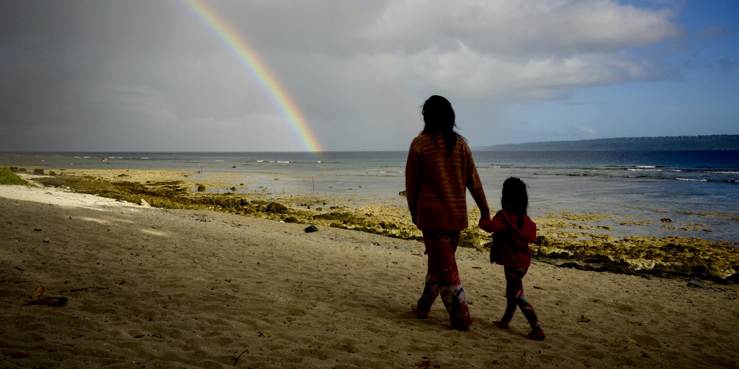 woman and child walk on beach with rainbow