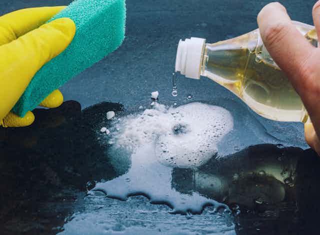 Close-up of hands holding a cleaning sponge and pouring vinegar onto fizzing bicarb.