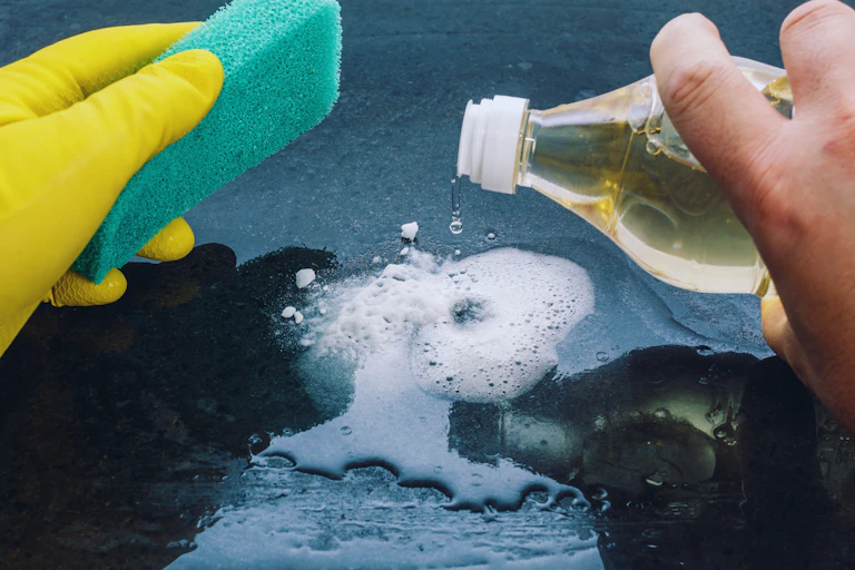 Close-up of hands holding a cleaning sponge and pouring vinegar onto fizzing bicarb.