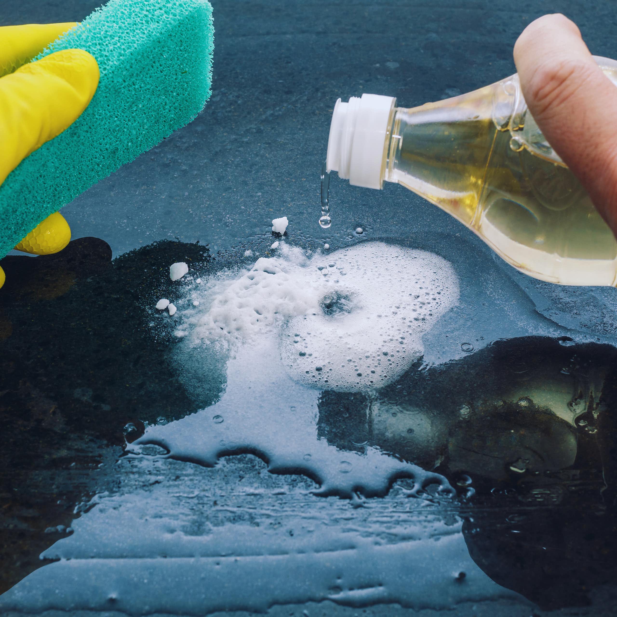 Close-up of hands holding a cleaning sponge and pouring vinegar onto fizzing bicarb.