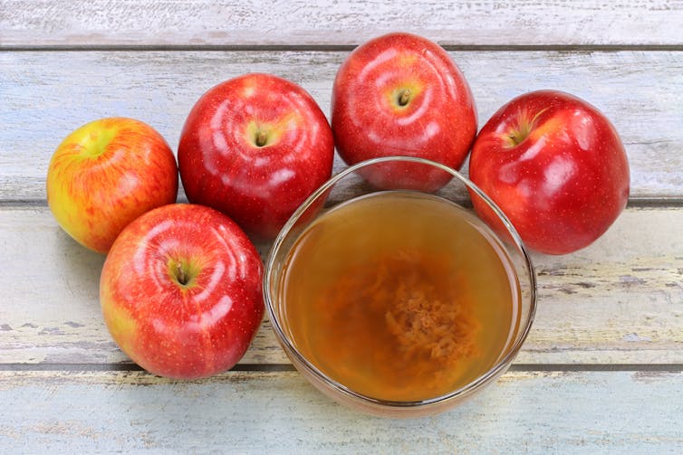 open glass of liquid with cloudy substance at bottom, surrounded by apples