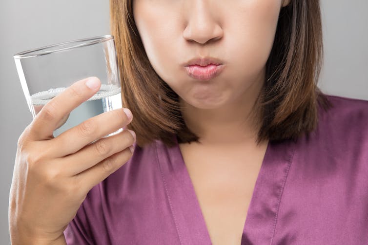 The woman is holding a glass of water and her cheeks are full.