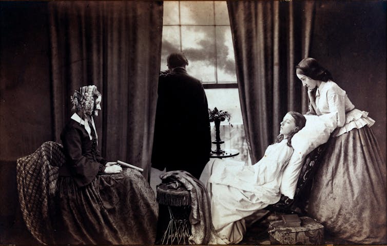 A black and white composite photo, showing a young woman lying sickly while another young woman stands behind her, and an older woman sits in a chair facing her. A silhouette of a man looks out the window. All are in Victorian-era clothing.