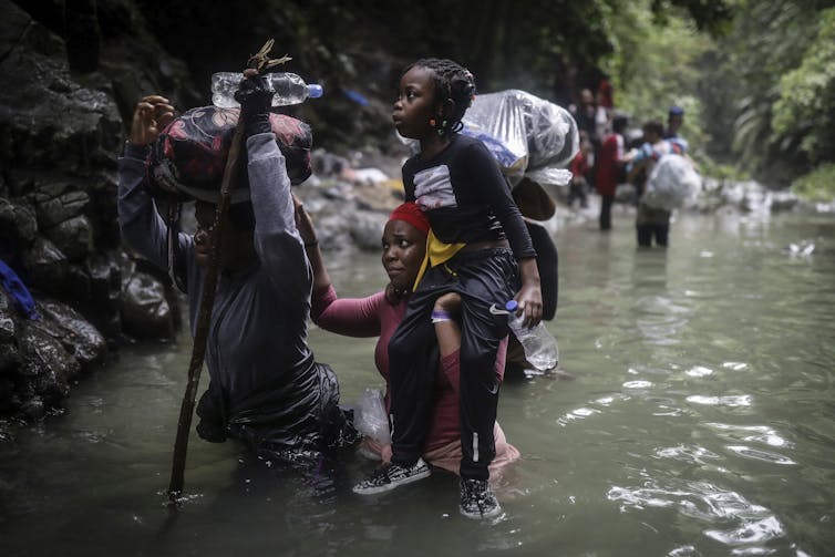 Un niño es izado sobre los hombros de un adulto mientras una mujer y un hombre caminan por el agua.