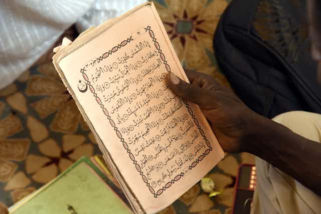Une main tient une page contenant un texte en lettres arabes.