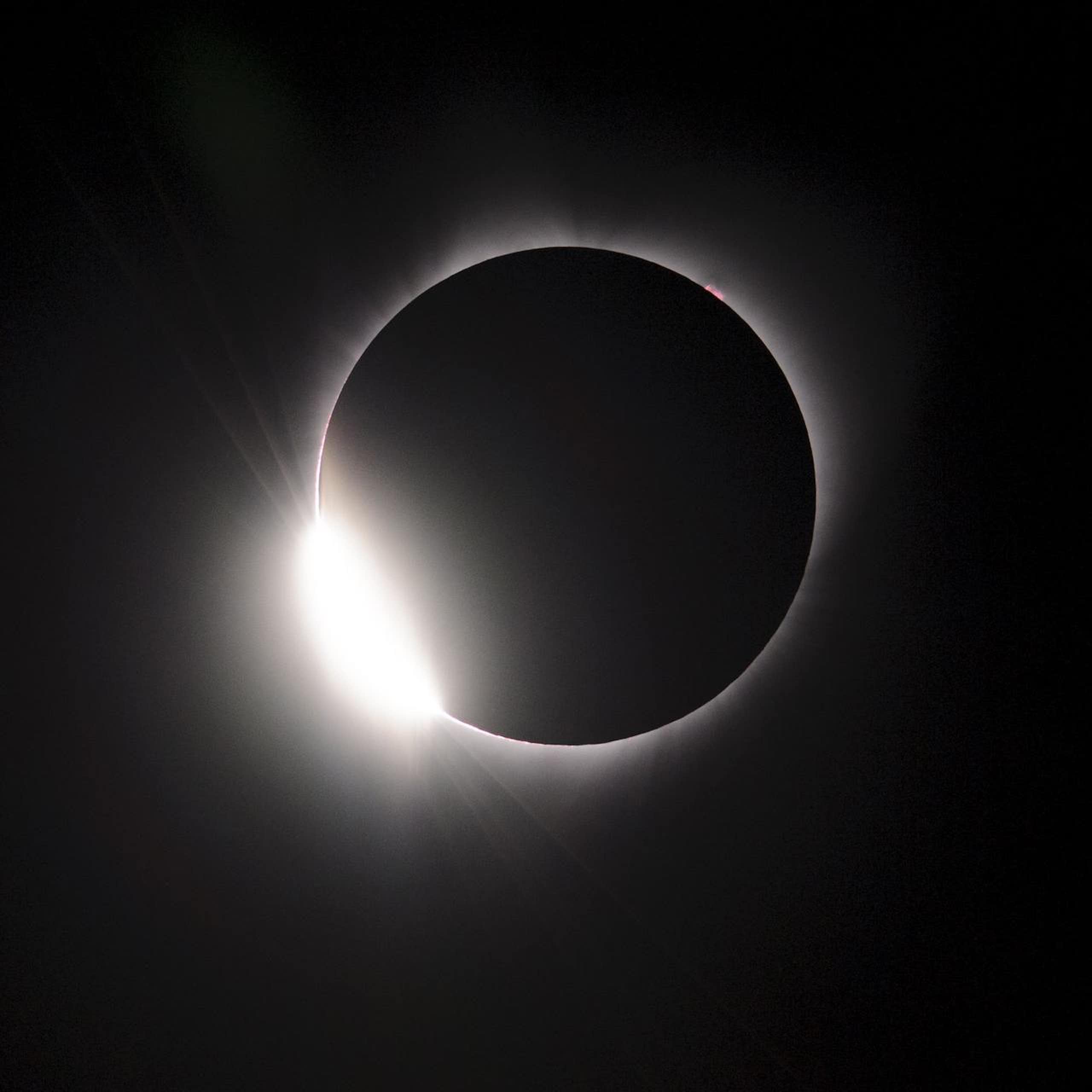 un cercle noir entouré d'un halo lumineux blanc sur fond sombre
