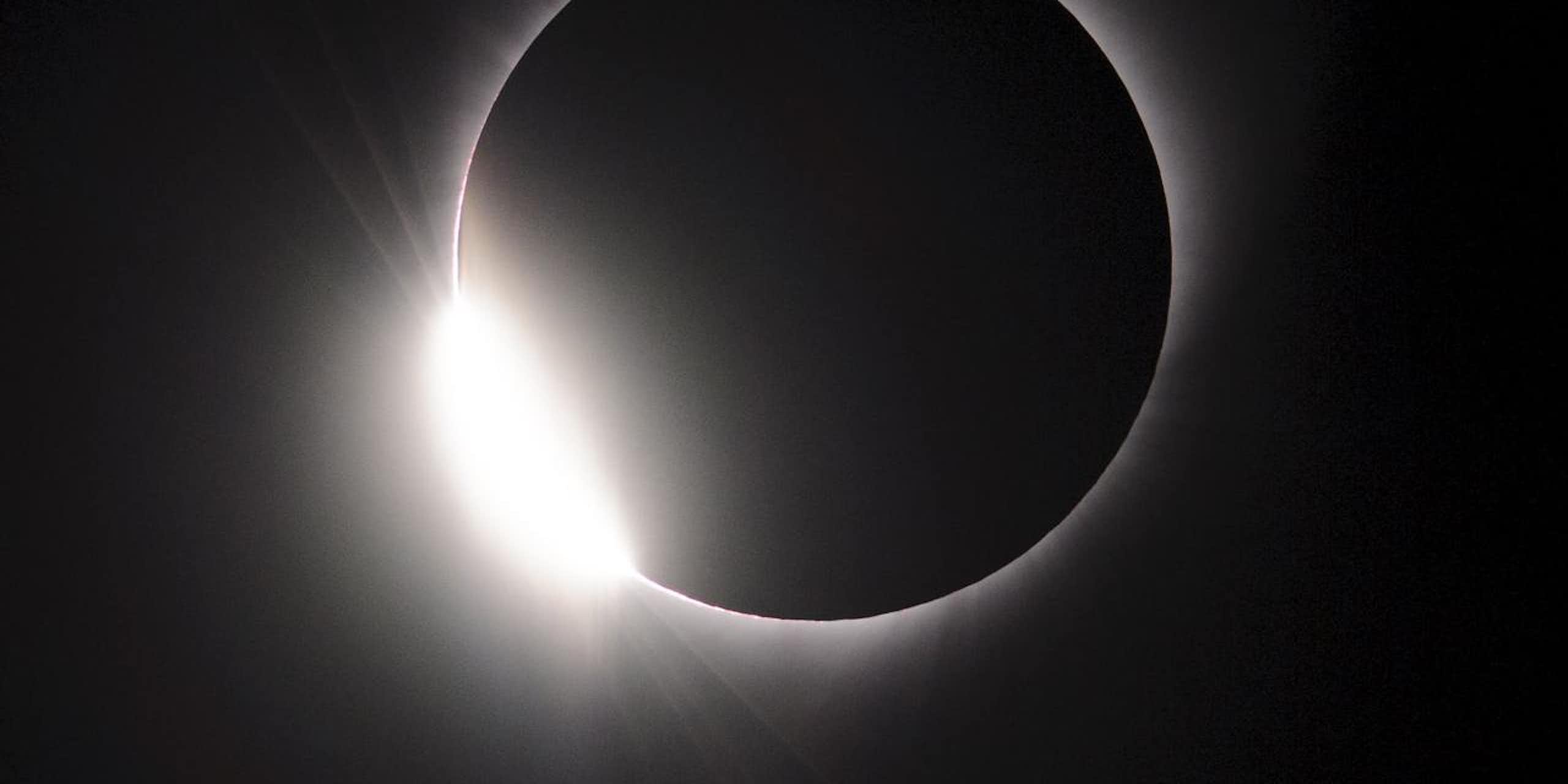 un cercle noir entouré d'un halo lumineux blanc sur fond sombre