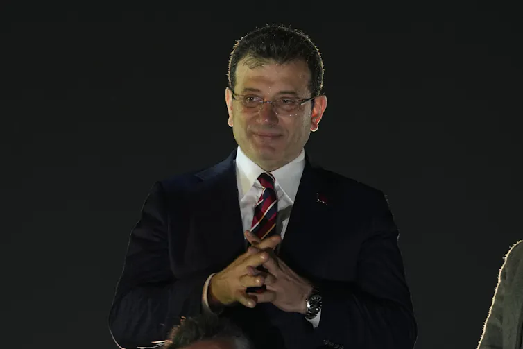A man in a dark suit with his hands clasped.