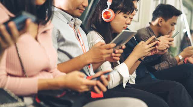 People sitting in a train check their mobile phones