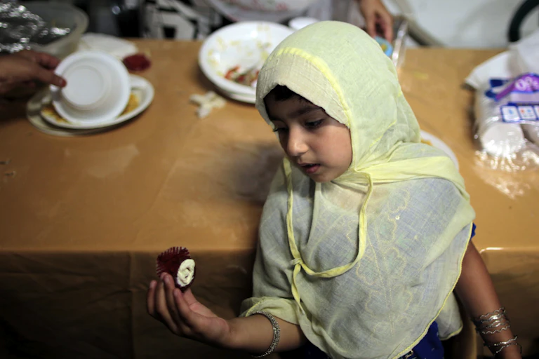 A young girl, with her head covered, sitting on a chair.