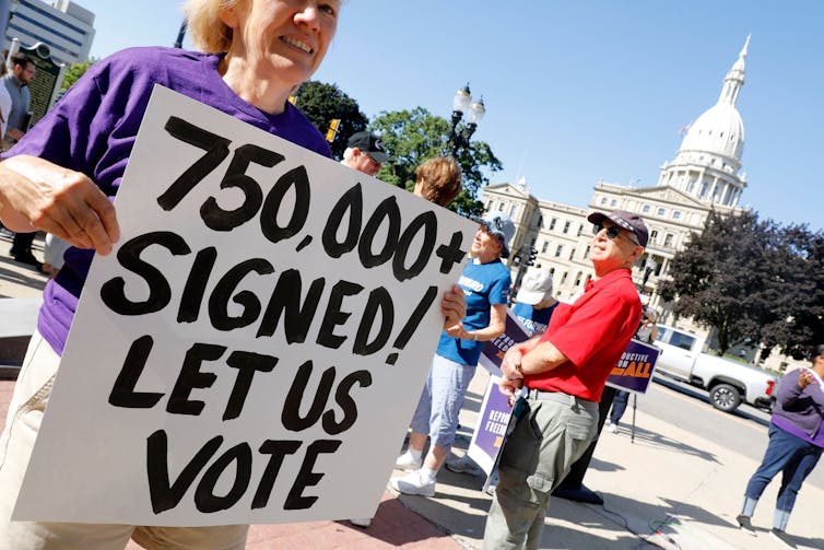 A woman at a protest holding a sign that says '750,000+ signed! Let us vote.'