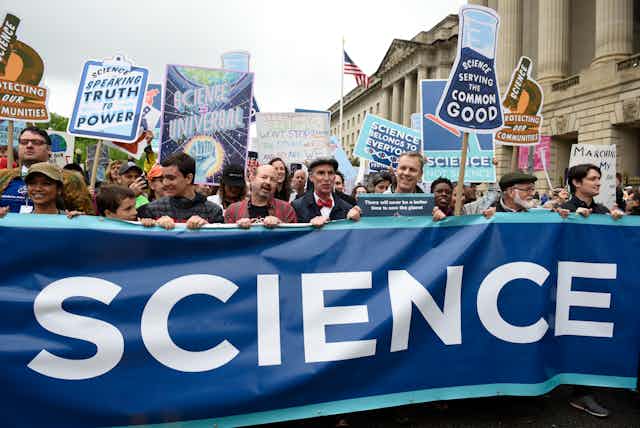people hold up small signs as well as a large banner with the word science displayed