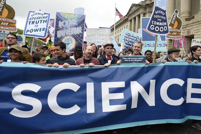 people hold up small signs as well as a large banner with the word science displayed