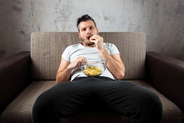 Homem sentado em um sofá comendo batatas fritas tiradas de uma tigela