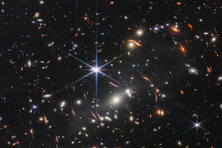 A photograph of the night sky, featuring gleaming pinpoints of white, blue and orange light.