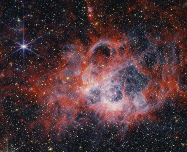 Des nuages de gaz et de poussières rouges, roses et blancs mettent en valeur ce paysage stellaire