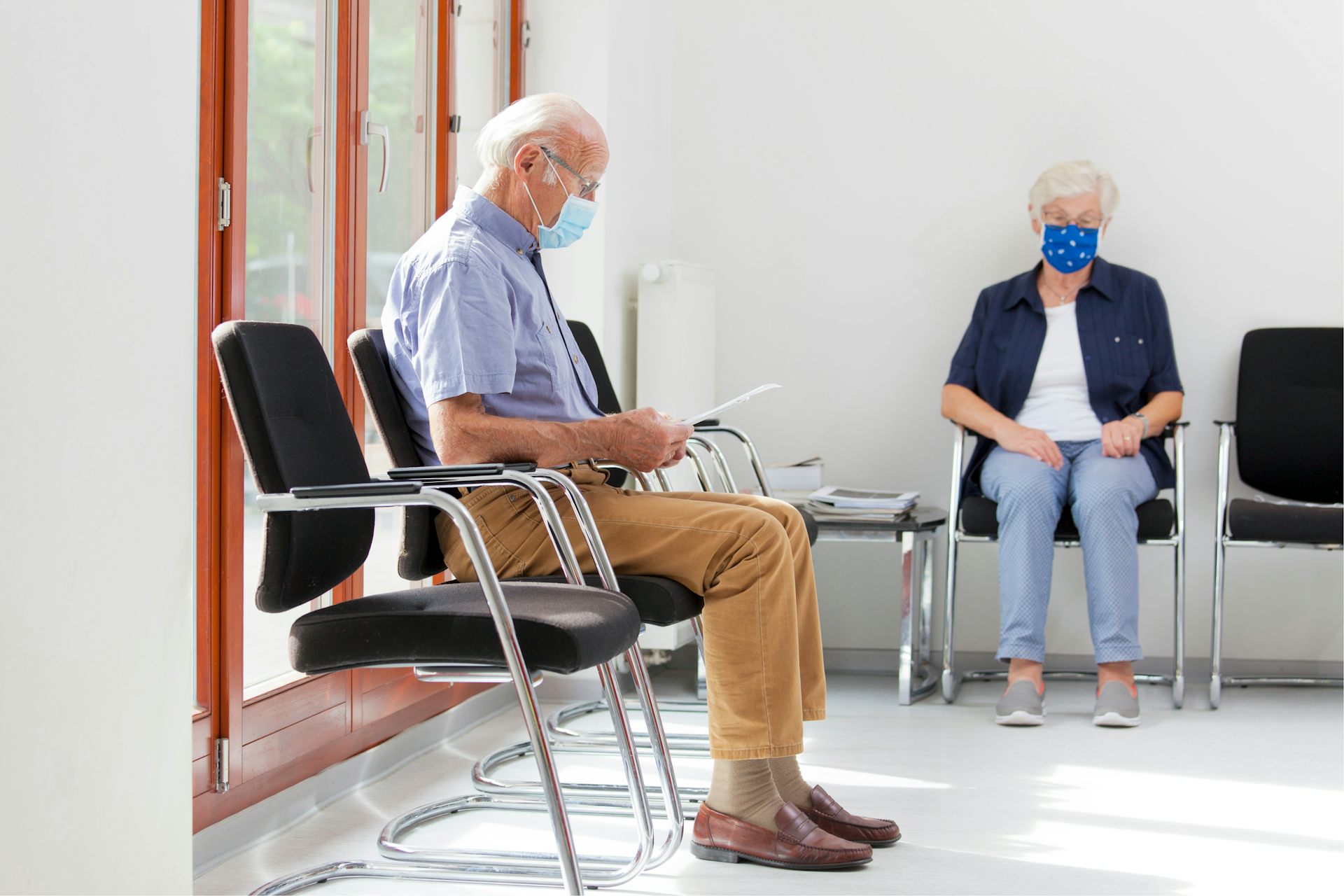 A man and woman sit in a brightly lit doctor's waiting room