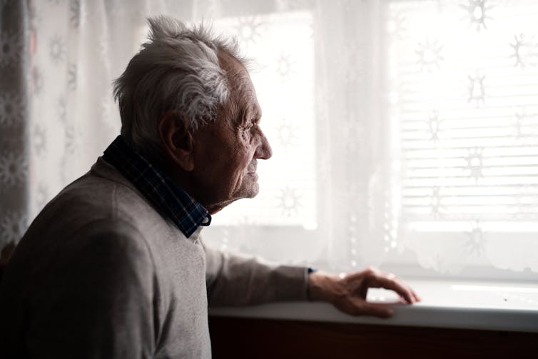 A senior man looks out a window.
