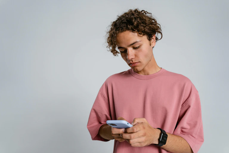 A teenage boy holds a phone against a blank background.