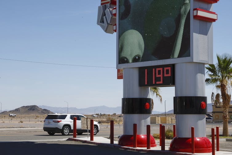 A car parked besidea giant thermometer showing 119 degrees farenheit (48°C).