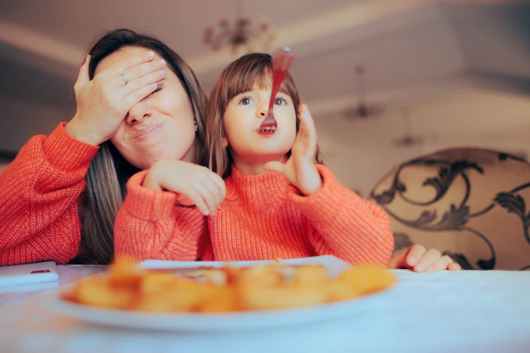 Mum with hand over eyes, with child playing with spoon in mouth