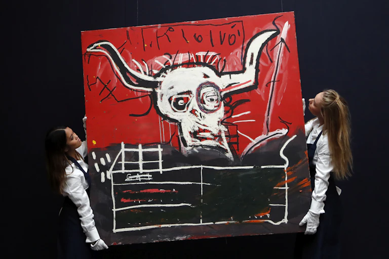 Two women carry a painting by Basquiat.