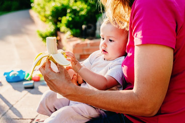 Mum with toddler on lap offering banana