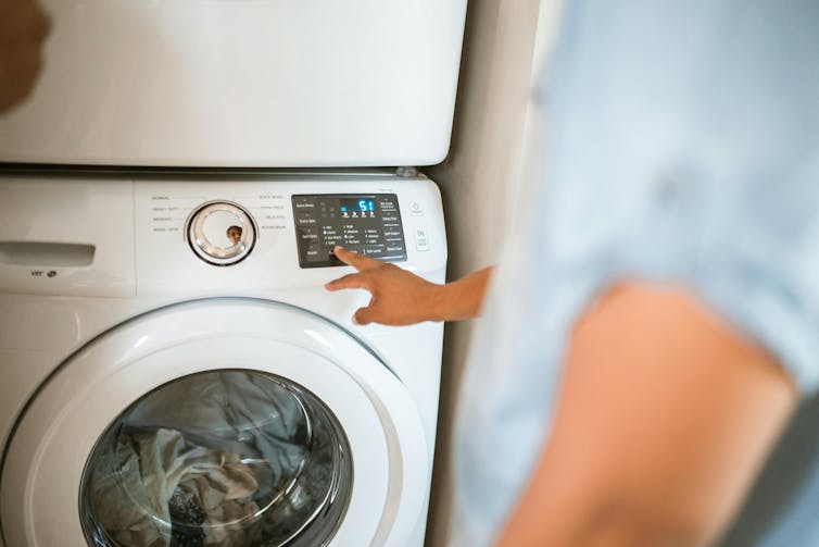 A person selecting a program on a front loader washing machine panel with buttons.