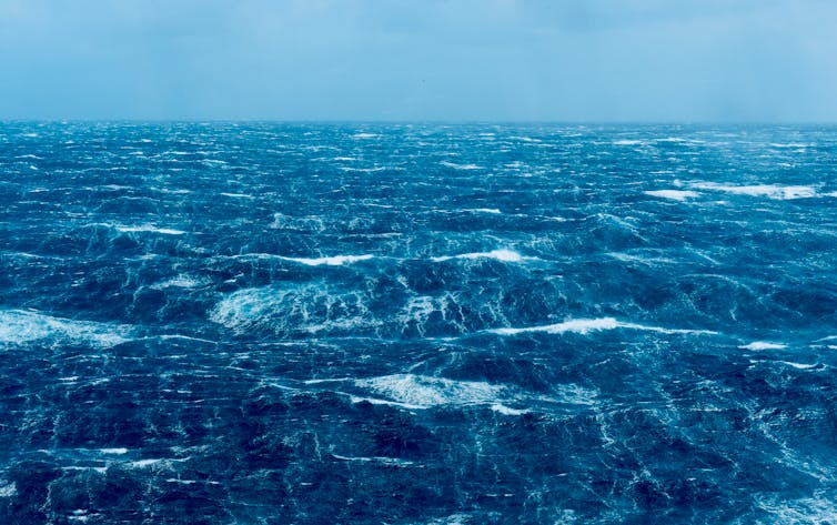 A blue coloured photo of the ocean surface with small white wave crests throughout.