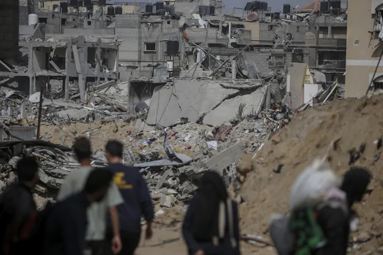 A group of people standing in the foreground of destroyed buildings.