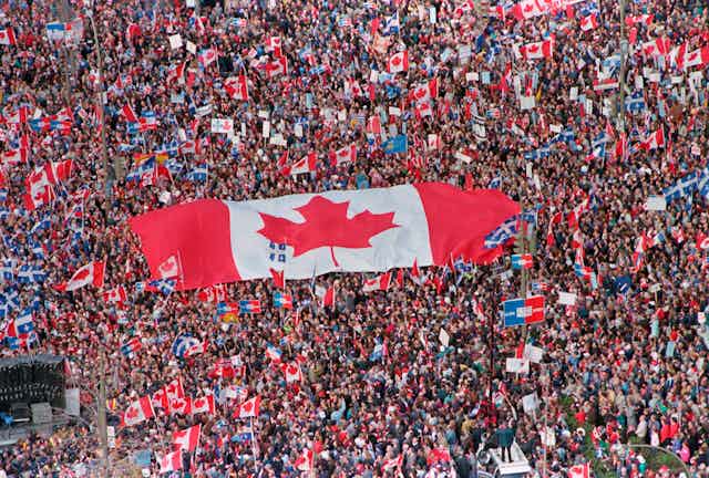 A large Canadian flag is seen being passed amid a huge crowd of people.