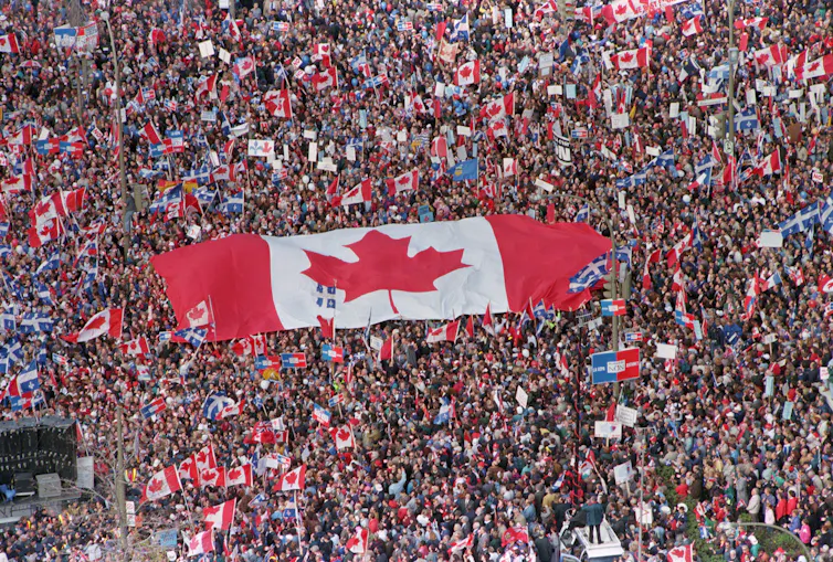 A large Canadian flag is seen being passed amid a huge crowd of people.