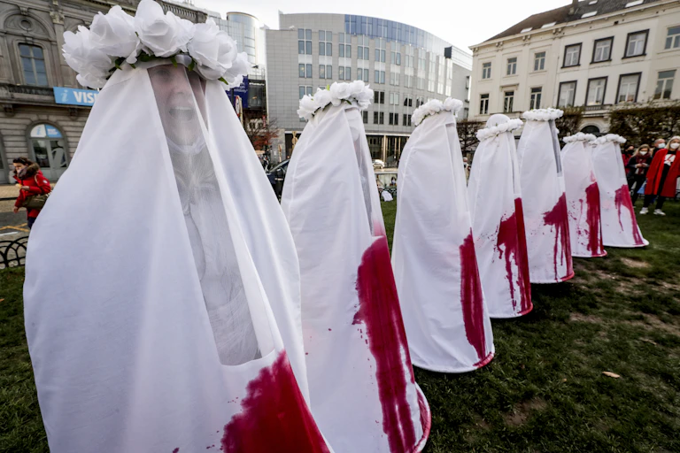 Women dressed in white costumes stained with blood stand in a line in Brussels.